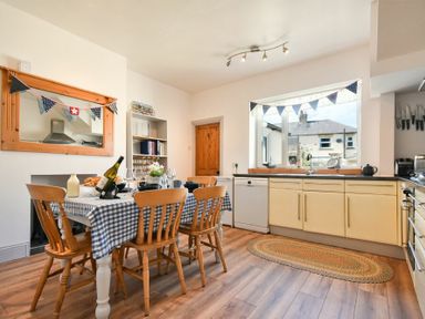 A kitchen with a dining table and six wooden chairs next to a window with bunting at Rosedale House in Amble