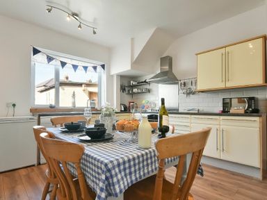 A kitchen with a wooden dining table covered with a blue checkered tablecloth and wooden chairs at Rosedale House in Amble