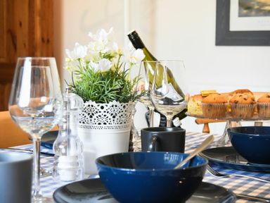 A dining table set with blue bowls black mugs wine glasses a white decorative flower pot and muffins on a cake stand at Rosedale House in Amble