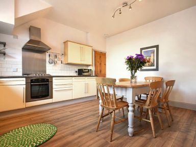 A kitchen with cream cabinets and a wooden dining table with five chairs and a vase of flowers at Rosedale House in Amble