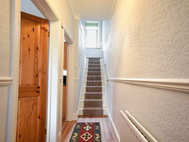 A hallway with wooden doors a striped carpet on stairs a patterned rug and a radiator at Rosedale House in Amble