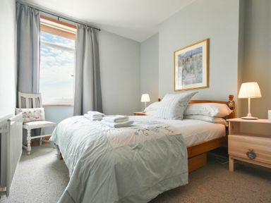 A bedroom with a bed pillows bedside tables lamps curtains and a chair at Rosedale House Amble