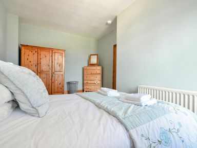 A bedroom with a bed made with white and blue bedding and folded towels on top with wooden wardrobe and chest of drawers at Rosedale House in Amble