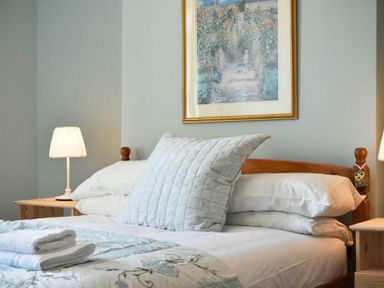 A bedroom with a wooden bed frame white pillows and blankets two bedside tables with lamps and a framed painting on the wall at Rosedale House in Amble