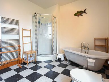 A bathroom with a corner shower, freestanding bathtub, toilet, towel rack, wooden chairs, and a fish decoration on the wall at Rosedale House in Amble