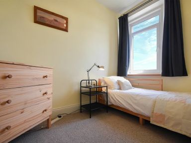 A bedroom with a single bed beside a window a small black bedside table with a lamp and a wooden chest of drawers at Rosedale House in Amble