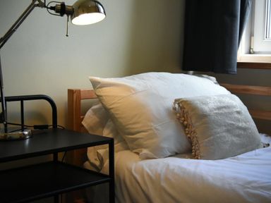 A bed with white pillows and a decorative cushion next to a black nightstand with a lamp by a window at Rosedale House in Amble