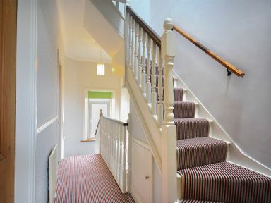 A hallway with striped carpeted stairs and floor and white banister at Rosedale House in Amble