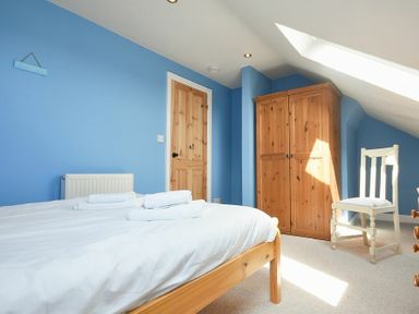 A bedroom with a wooden bed with white bedding a wooden wardrobe a white chair and a wooden door at Rosedale House in Amble