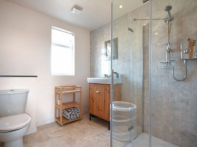 A bathroom with a toilet wooden shelving unit a sink with cabinet and a shower at Rosedale House in Amble