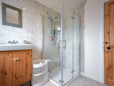 A bathroom with a glass shower enclosure wooden vanity unit with sink round laundry basket and wooden door at Rosedale House in Amble