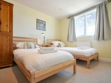 A bedroom with two single beds a wooden wardrobe and a window with curtains at Rosedale House in Amble