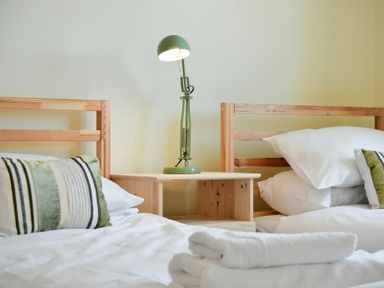 A bedroom with two wooden beds separated by a wooden nightstand with a green lamp at Rosedale House in Amble