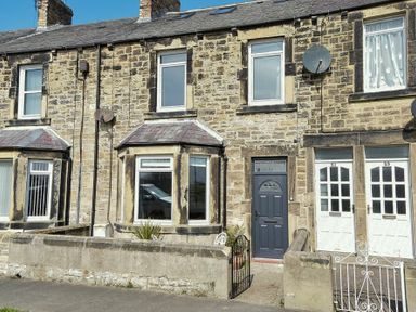A stone terraced house with bay windows and a dark front door with a small front garden at Rosedale House in Amble