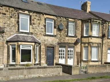 Exterior of a stone terraced house with bay windows satellite dishes and a small garden area in front at Rosedale House in Amble