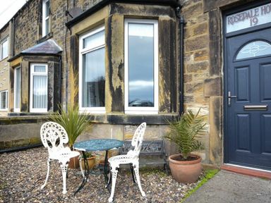 A stone house exterior with a blue door number 19 white chairs a blue table and potted plants at Rosedale House in Amble
