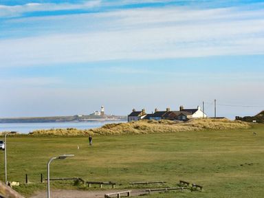 A grassy field with a person and dog near houses and a lighthouse by the water at Rosedale House in Amble