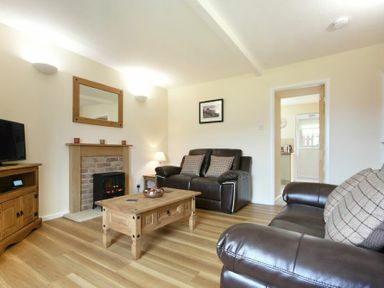 A living room with brown leather sofas a wooden coffee table a fireplace and a television at Dryden Cottage in Bamburgh