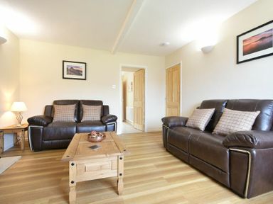 A living room with two brown leather sofas wooden coffee table wooden side table and framed pictures on walls at Dryden Cottage Bamburgh