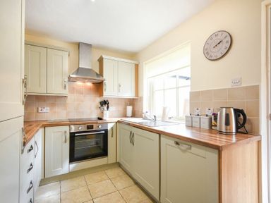 A kitchen with cabinetry a stove oven hood a sink kettle and containers at Dryden Cottage Bamburgh