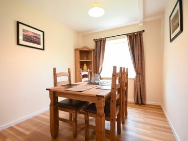 A dining room with wooden table and chairs a cabinet and window with curtains at Dryden Cottage Bamburgh