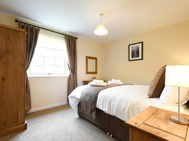 A bedroom with bed bedside table lamp window wardrobe and framed picture at Dryden Cottage in Bamburgh
