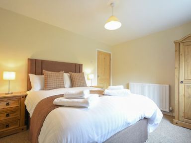 A bedroom with a double bed cushions bedside tables lamps a wooden wardrobe and a radiator at Dryden Cottage Bamburgh