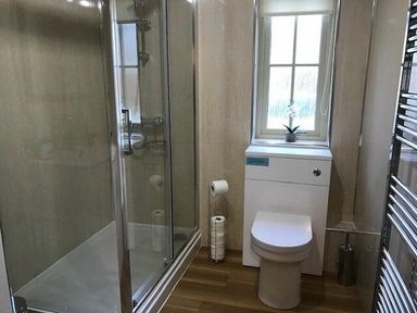 A bathroom with a shower enclosure a toilet a window with a plant on the sill and a towel radiator at Dryden Cottage in Bamburgh
