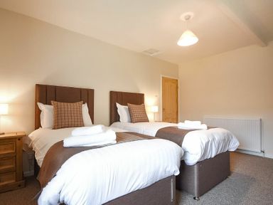 A bedroom with two single beds bedside tables lamps and folded towels at Dryden Cottage in Bamburgh