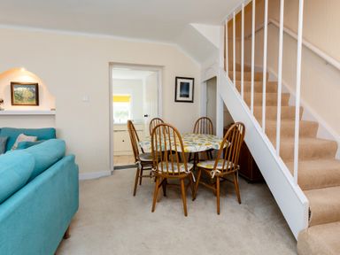A dining area with a table and six chairs next to carpeted stairs and a blue sofa in a living room at Percy Cottages No4 in Alnmouth