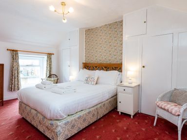 A bedroom with a double bed bedside table two chairs floral curtains and wallpaper at Percy Cottages No4 in Alnmouth