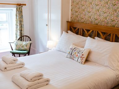 A bedroom with a wooden bed headboard white bedding floral pillow and curtains at Percy Cottages No4 in Alnmouth
