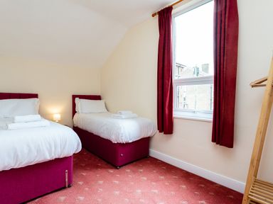 A bedroom with two single beds white bedding red headboards and curtains a window and a wooden clothes rack at Percy Cottages No4 in Alnmouth