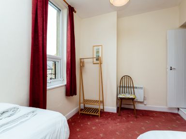 A bedroom with a window with red curtains a wooden chair a wooden clothing rack and a bed at Percy Cottages No4 in Alnmouth