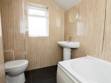 A bathroom with a toilet sink bathtub window and circular mirror at Percy Cottages No4 in Alnmouth