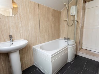 A bathroom with a white pedestal sink bathtub with a shower and glass screen at Percy Cottages No4 in Alnmouth