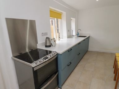 A kitchen with a stove, blue cabinets, countertop with a kettle and sink at Percy Cottages No4 in Alnmouth