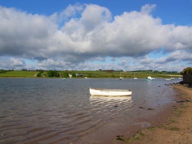 A boat on the water with green land and clouds at Percy Cottages No4 Alnmouth