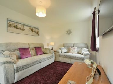 A living room with two grey sofas purple cushions and a wooden table at The Chevy in Seahouses