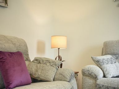 A living room with two grey armchairs with cushions and a lamp on a side table between them at The Chevy in Seahouses