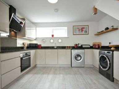 A kitchen with built in oven washing machine and dryer with wall cabinets and a window at The Chevy in Seahouses