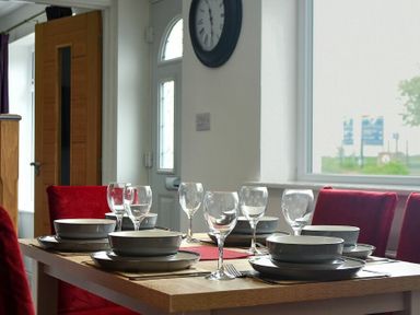 A dining table set with bowls glasses and cutlery with red chairs near a window at The Chevy in Seahouses