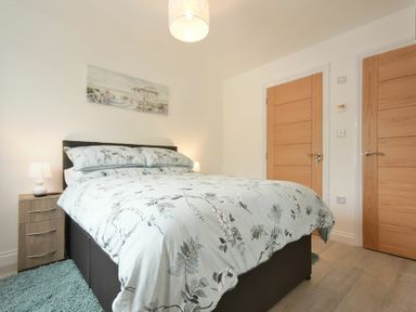A bedroom with a bed with floral bedding two wooden doors and a bedside table with lamps at The Chevy in Seahouses