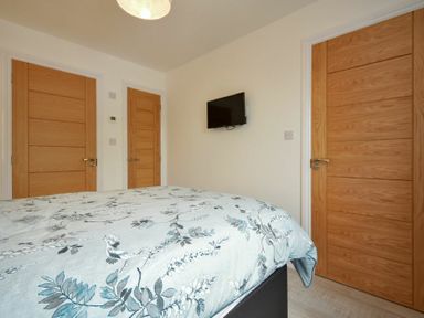 A bedroom with a bed covered in a floral patterned duvet and three wooden doors with a wall-mounted television at The Chevy in Seahouses