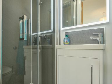 A bathroom with a glass shower enclosure a white sink with a faucet a soap dispenser and a mirror at The Chevy in Seahouses