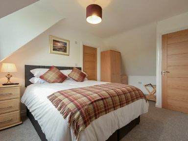 A bedroom with a bed with plaid throws and pillows a wooden wardrobe bedside table with lamp and two wooden doors at The Chevy in Seahouses