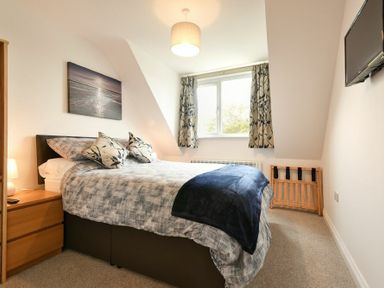 A bedroom with a bed bedside table lamp window and wall-mounted television at The Chevy in Seahouses