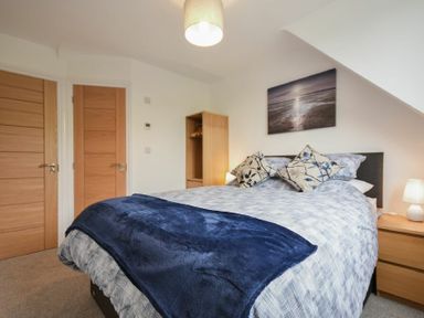 A bedroom with a bed covered in blue and white bedding two wooden doors a wooden wardrobe and a bedside table with a lamp at The Chevy in Seahouses