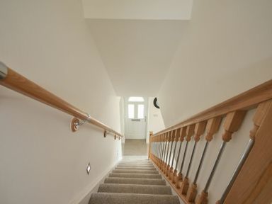 A carpeted staircase with wooden handrails and metal balusters leading down to a white front door at The Chevy in Seahouses