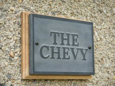 A metal sign with the text The Chevy mounted on a wooden board and attached to a pebble wall at The Chevy in Seahouses